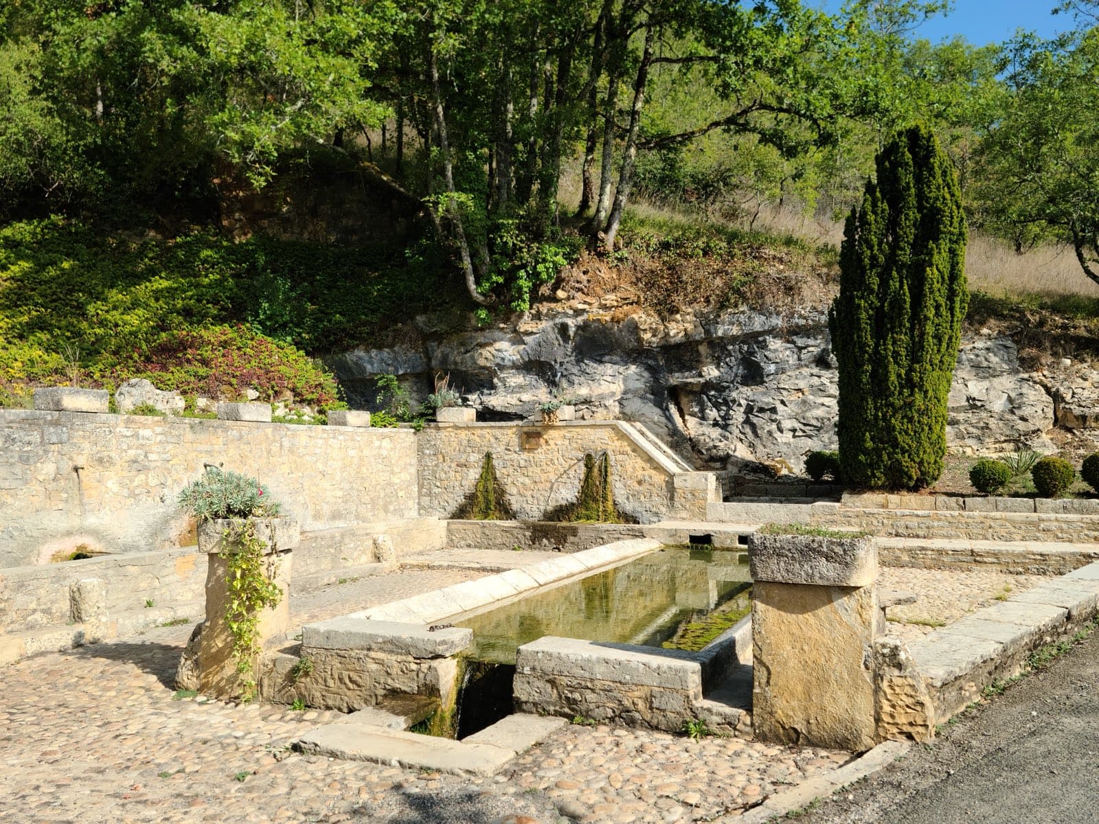 La fontaine et le lavoir de Nuzéjouls, son bassin de pierre alimenté par la source, au pied de la falaise